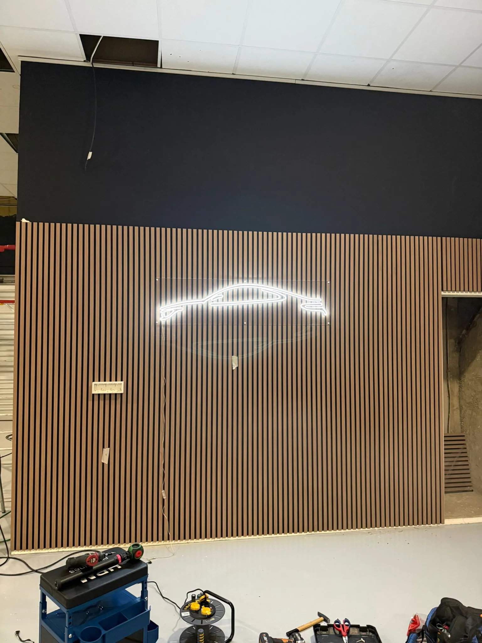 Pared revestida de lamas de madera con la silueta de un coche deportivo dibujada mediante tira LED retroiluminada